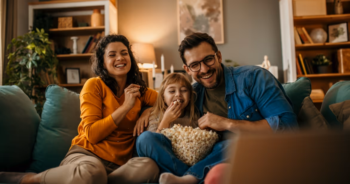 a family sitting on a couch watching a movie with popcorn to represent the introduction to fostering info session with Origins