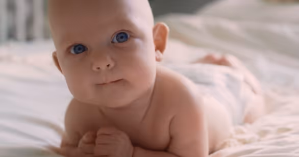 Close-up of a content baby with blue eyes lying on a soft bed, representing the safe, loving home environment provided by foster carers in Ireland which they can do when they understand the benefits of slowing down in foster care.