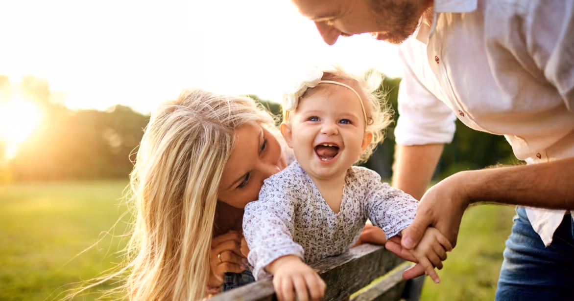 a blonde smiling baby and two parents on a park bench representing having a place to belong for a child in foster care