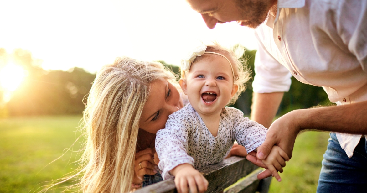 a blonde smiling baby and two parents on a park bench representing having a place to belong for a child in foster care