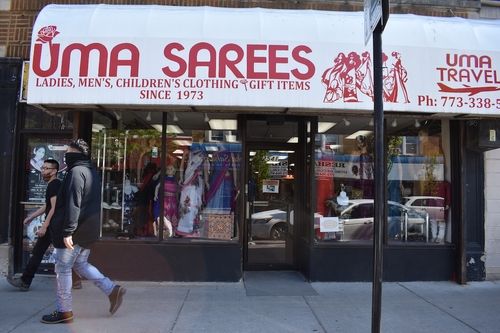 An image of two people walking in front of a storefront with a white awning and "Uma Sarees" in red text.