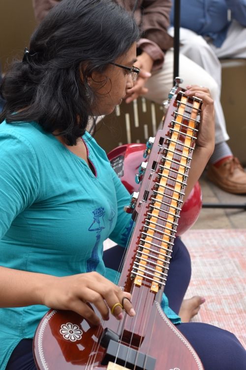 Women wearing a turquoise shirt sitting on floor playing a veena.
