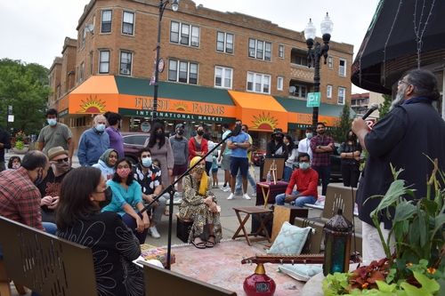 Image of a crowd of people gathered for an Aao Mil event on a street corner on Devon Avenue.