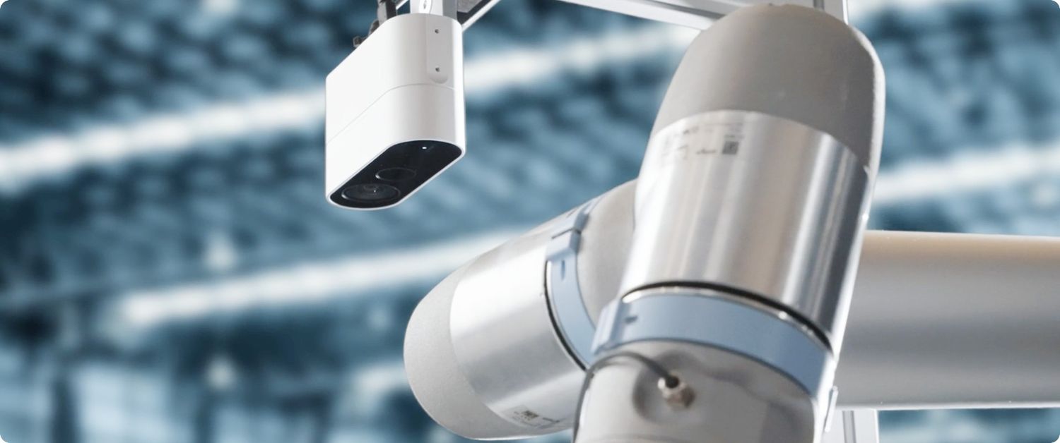 Eine Industriekamera ist über einem Roboterarm positioniert und ermöglicht durch bildbasierte Automatisierung das präzise Erkennen und Greifen von Objekten.