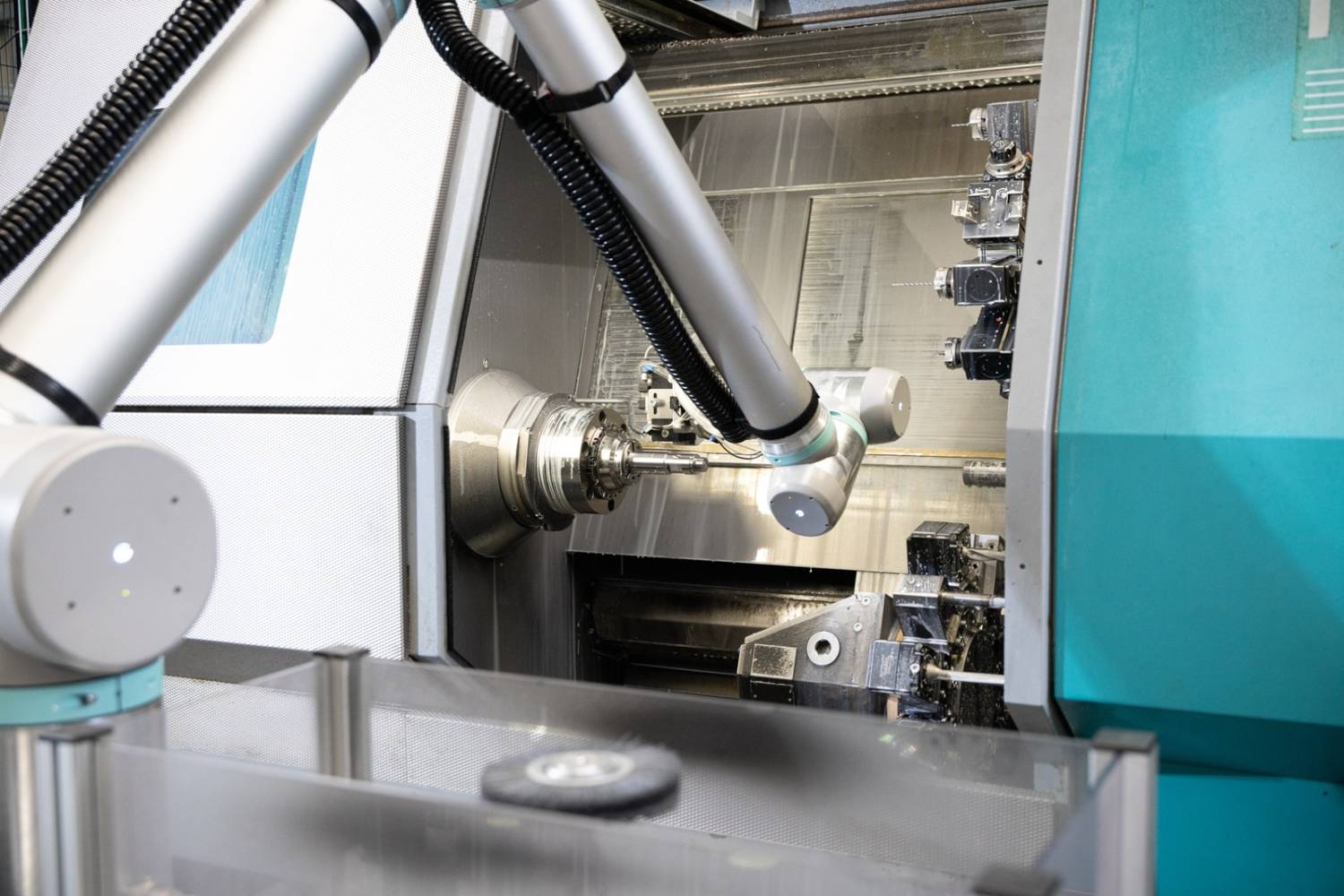 Ein Roboter für eine Drehmaschine legt präzise und automatisiert ein Bauteil in die Spannvorrichtung einer CNC-Drehmaschine ein, um den Fertigungsprozess zu optimieren.