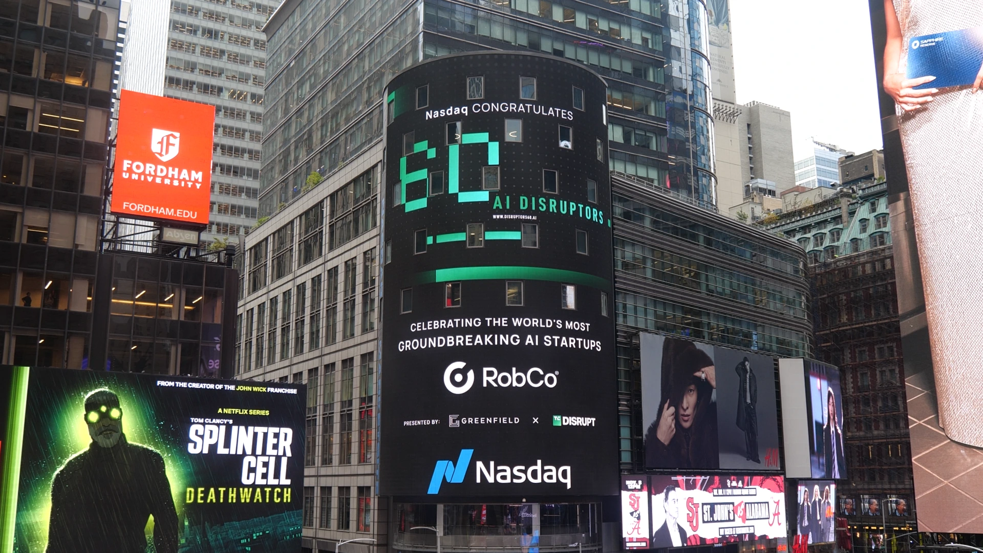 A large Nasdaq billboard in Times Square, New York, displays a message congratulating the “60 AI Disruptors,” featuring RobCo as one of the world’s most groundbreaking AI startups. The ad includes the Nasdaq and TechCrunch Disrupt logos, surrounded by other bright digital billboards.