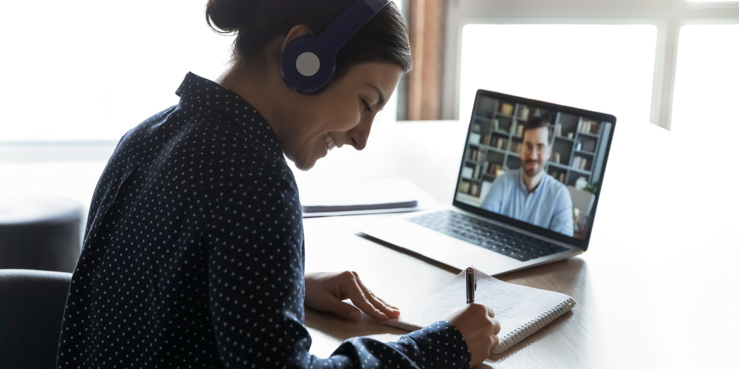 Woman wearing headphones taking notes during a virtual webinar on a laptop with a speaker discussing HOA regulations and AB 130 changes