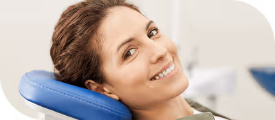 Smiling woman reclining on a blue dental chair in a clinic setting.