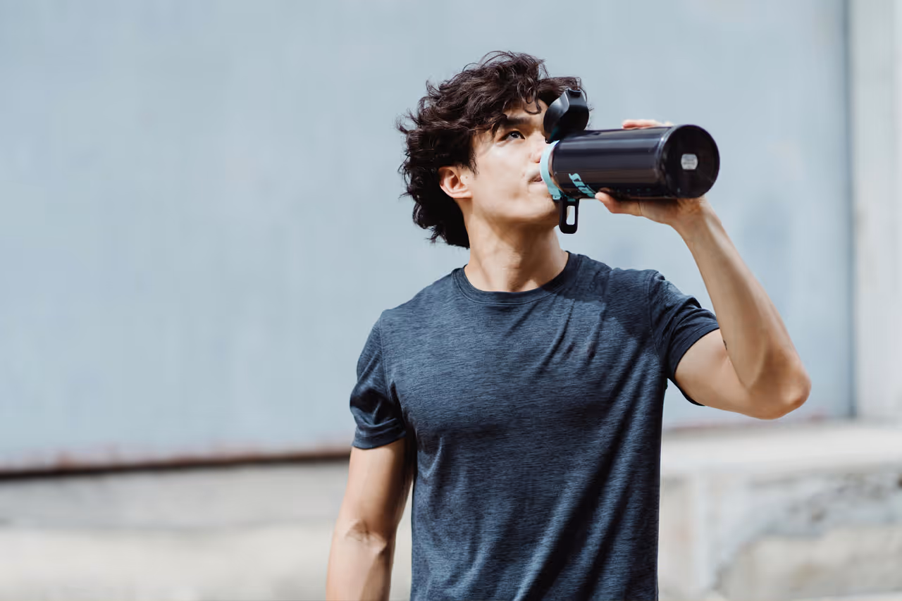 Young man in t shirt drinking from a large flask