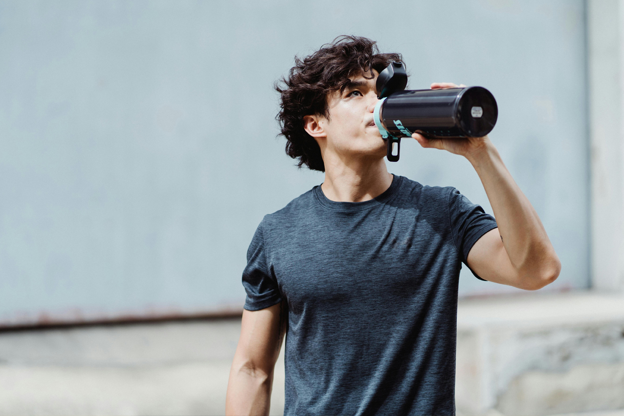 Young man in t shirt drinking from a large flask
