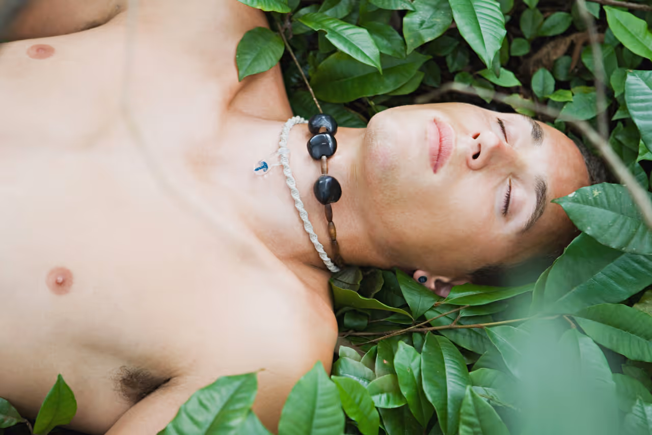Man with no shirt lying amongst green plants