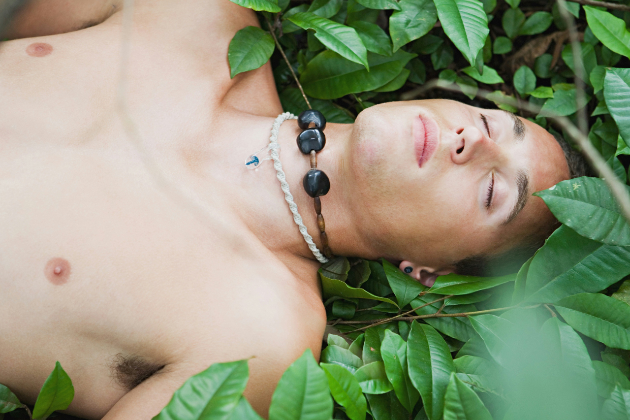 Man with no shirt lying amongst green plants