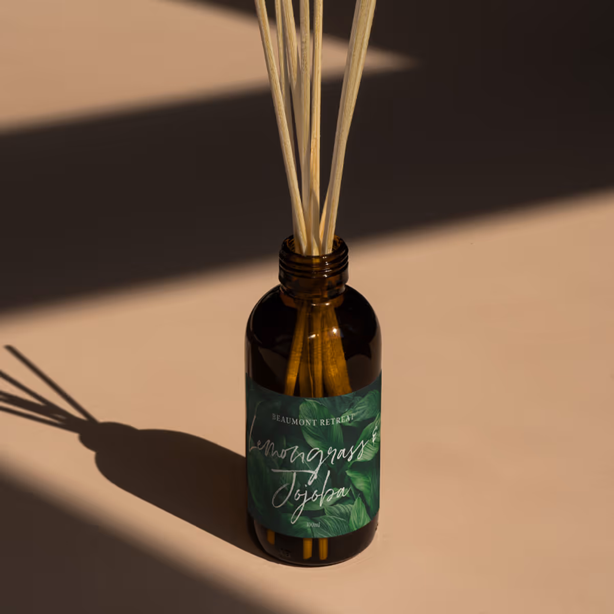 Bottle of lemongrass jojoba reed diffuser casting shadow on beige surface.