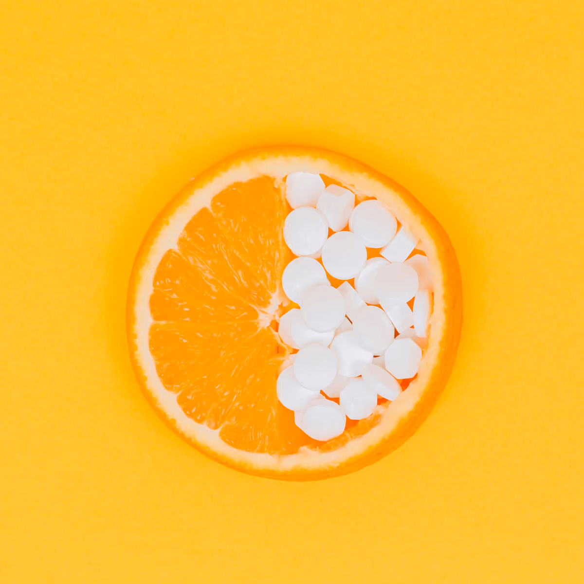 Half an orange with white supplement tablets filling the other half on a yellow background.