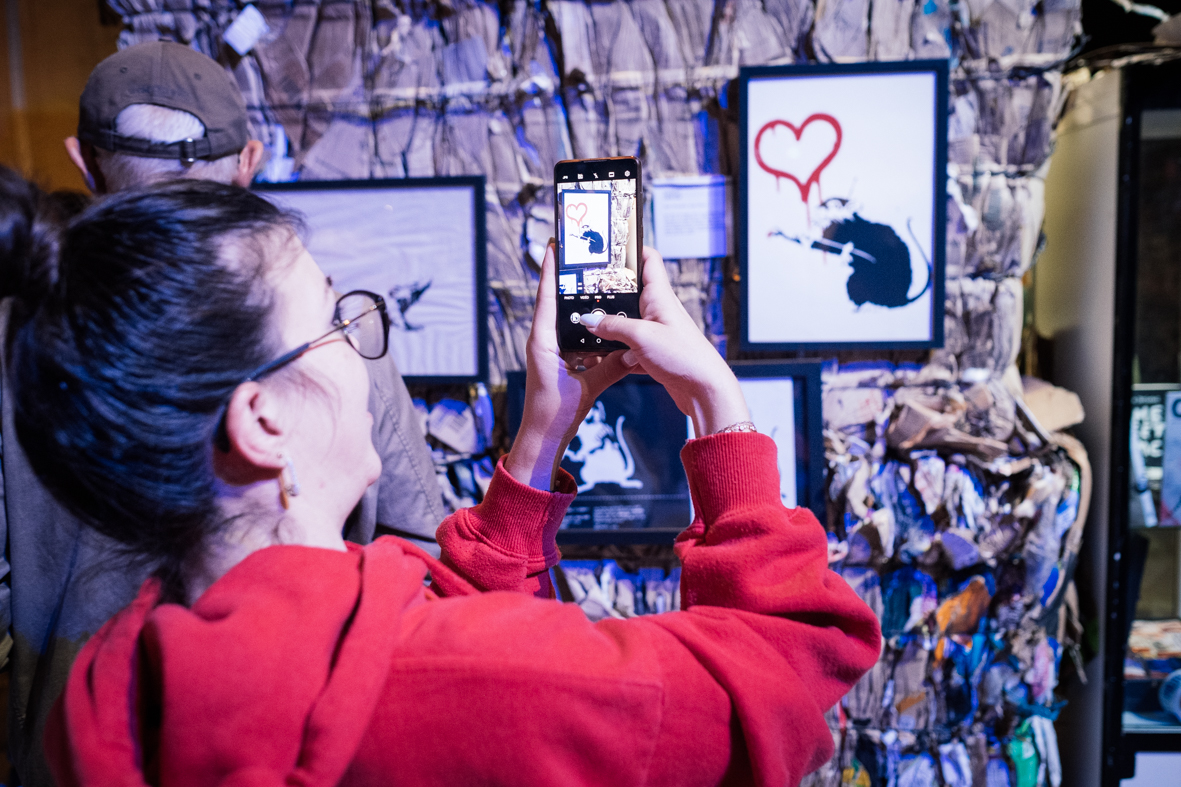 Besucherin fotografiert ein Banksy-Werk in der Ausstellung