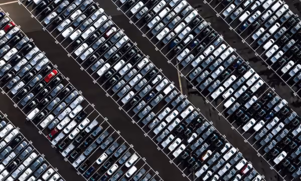 Aerial view of multiple rows of parked cars in a lot, mostly white and black with a few red cars.