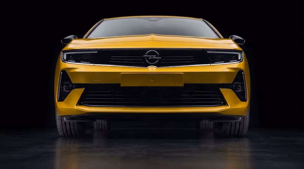 Front view of a yellow Opel car with black grille and headlights on a black background.