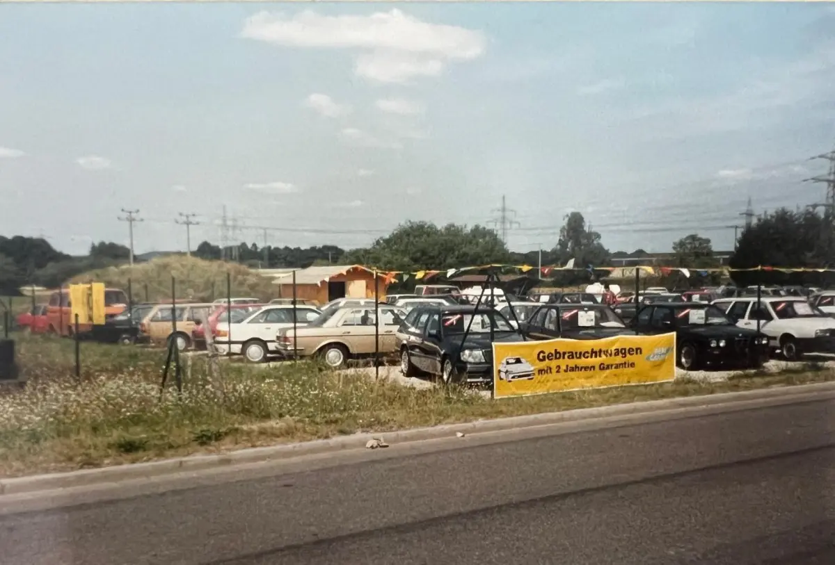 Used cars parked behind a fenced lot with a yellow banner advertising a 2-year warranty.