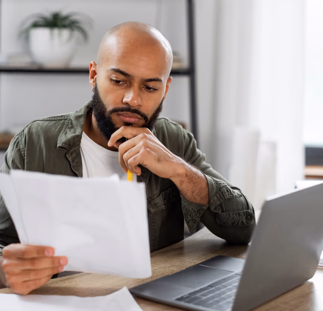 A thoughtful young man examines a sheet of paper adorned with questions he's penned, preparing to seek guidance from a Tandem customer support agent regarding his loan repayment options.