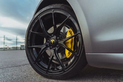 Close-up of a black aftermarket wheel with yellow brake calipers on a Tesla.