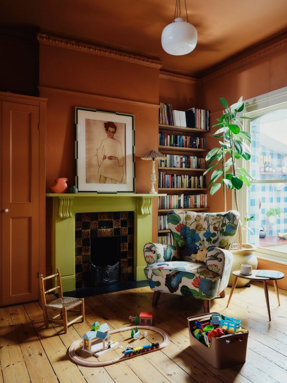 The finished play room: terracotta walls, a green fireplace and a vintage patterned armchair