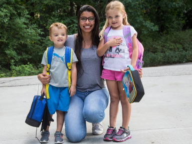 An au pair kneeling down taking a picture with her two host kids as they go off to school. 
