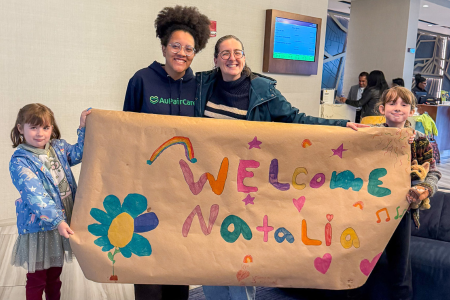 An au pair and her host family holding a sign that says "welcome Natalia"