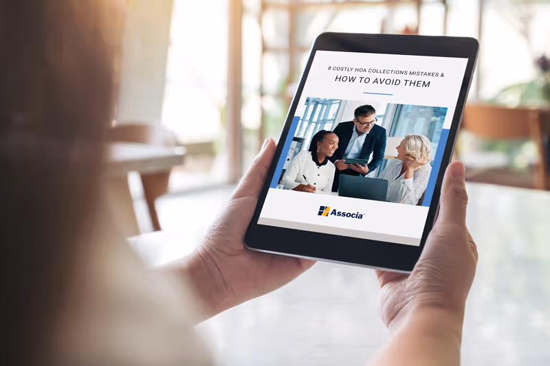 Tablet screen showing an ebook titled '8 Costly HOA Collections Mistakes & How to Avoid Them' with a photo of three smiling professionals in discussion and Associa logo below.