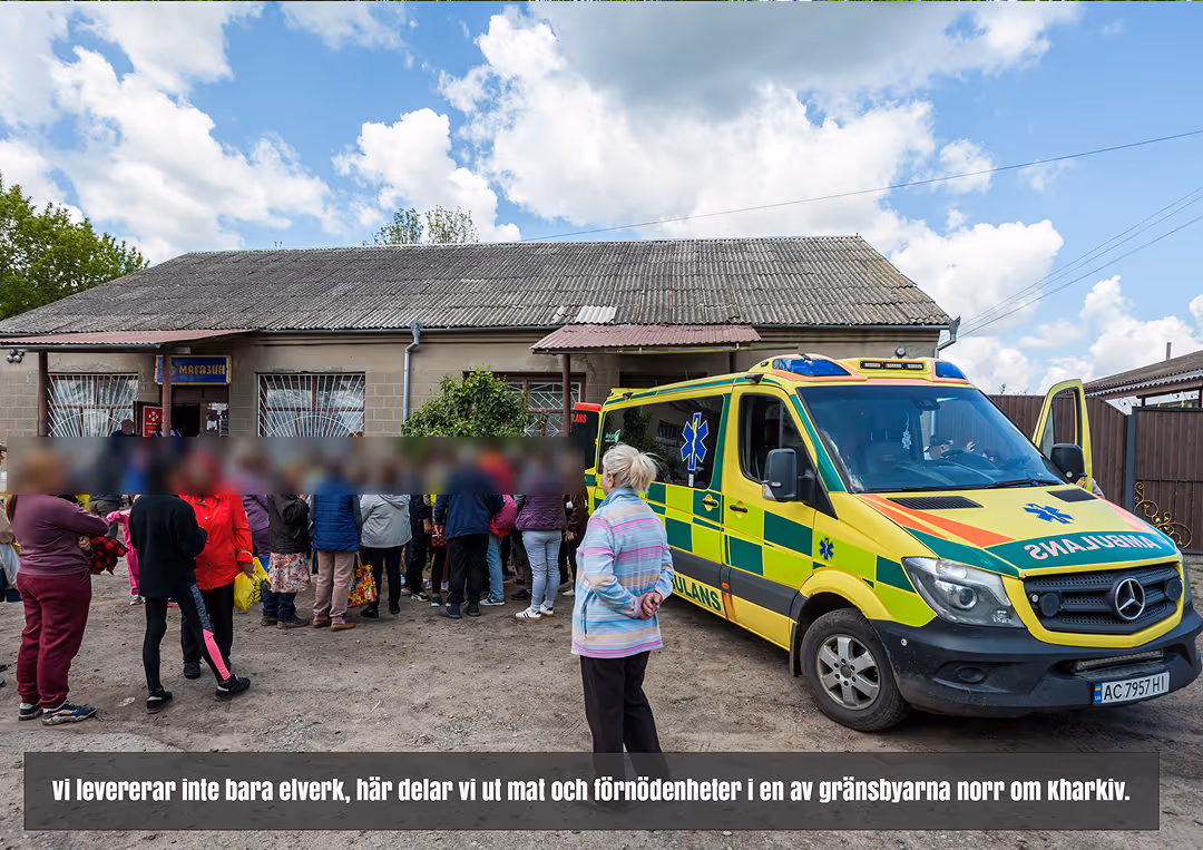 En ambulans parkerad bredvid en grupp människor som samlas utanför en byggnad under en molnig himmel.