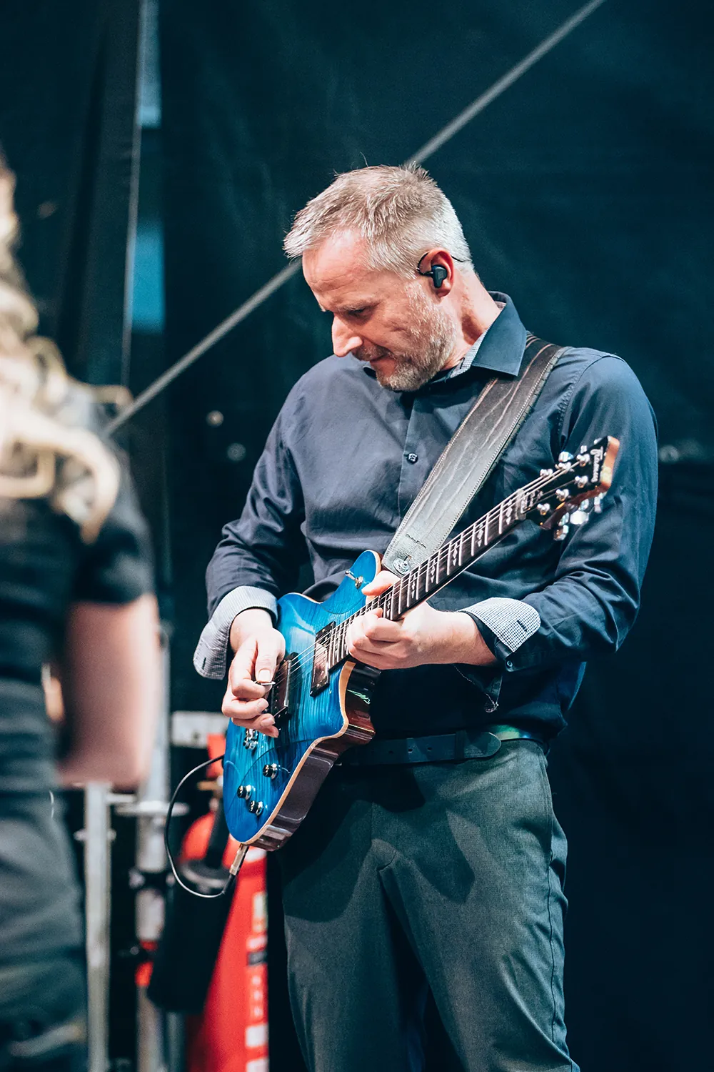 Man wearing dark blue shirt playing a blue electric guitar on stage.