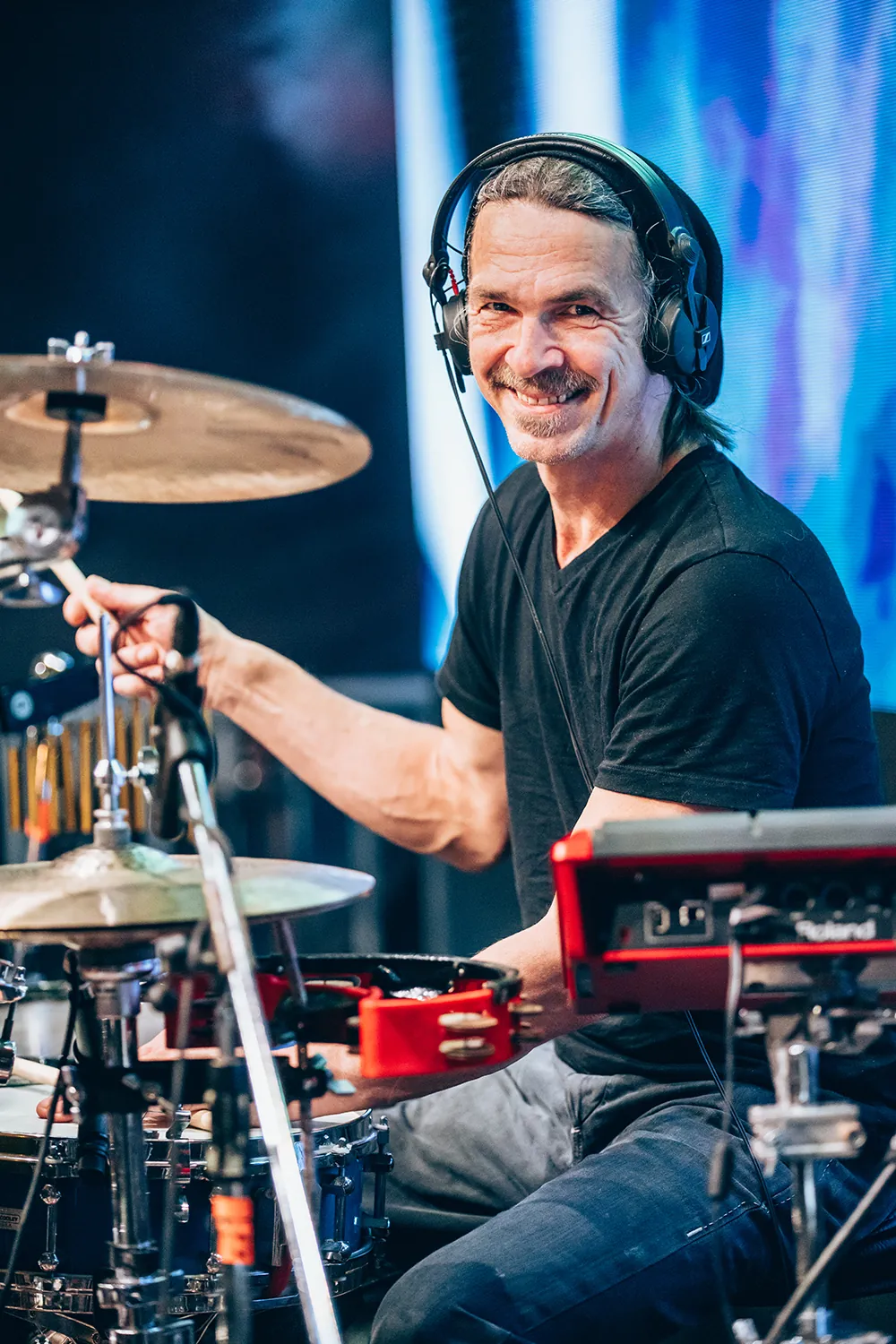 Male drummer wearing headphones smiling while playing drums on stage.