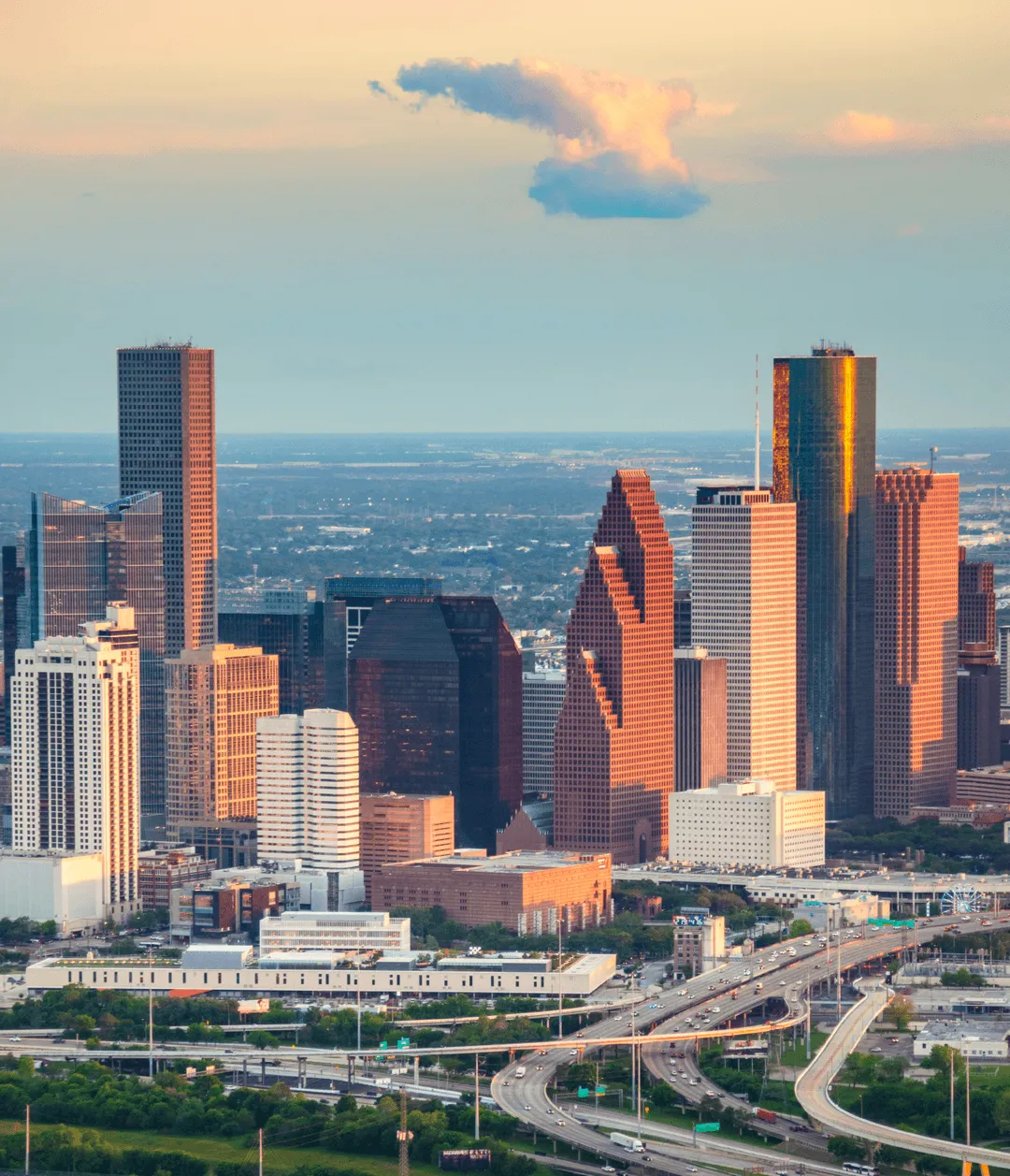 Aerial view of the Houston skyline at sunset, showcasing modern skyscrapers and busy highways with a colorful sky in the background.
