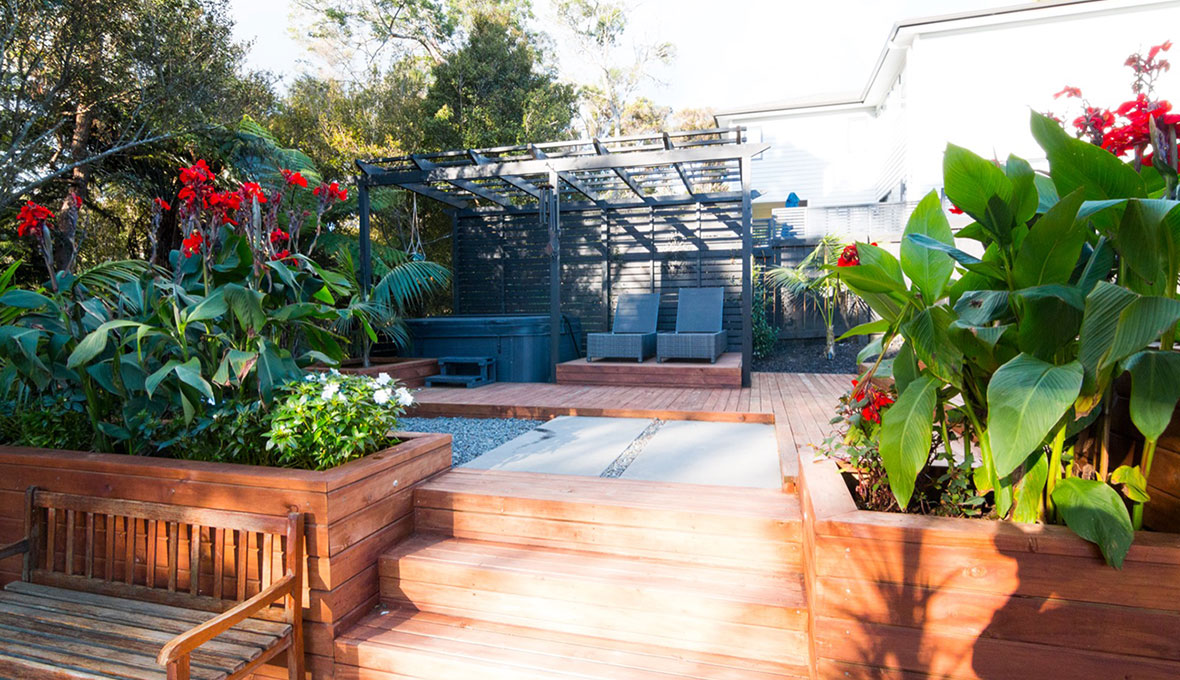 Sloped New Zealand garden with terraced levels, retaining walls, planting, and outdoor seating areas