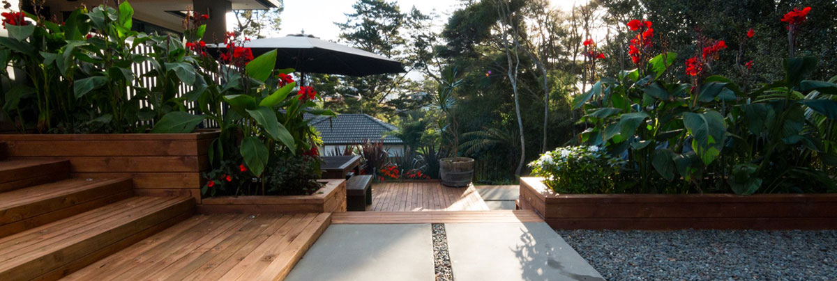 Sloped New Zealand garden with terraced levels, retaining walls, planting, and outdoor seating areas