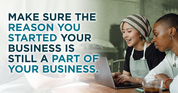 Three people sitting at a table in a cafe with a laptop and notebooks. One person is taking notes while another is typing on the laptop. The overlay of words reads "Make sure the reason you started your business is still a part of your business."