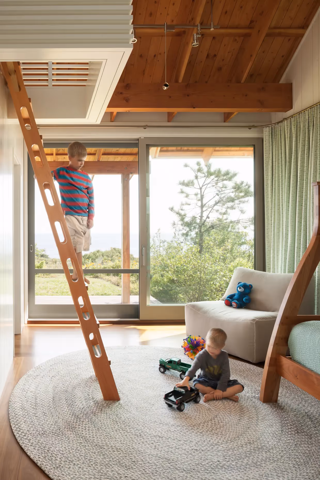 Two children playing with toys in bright, wooden-beamed room with large windows