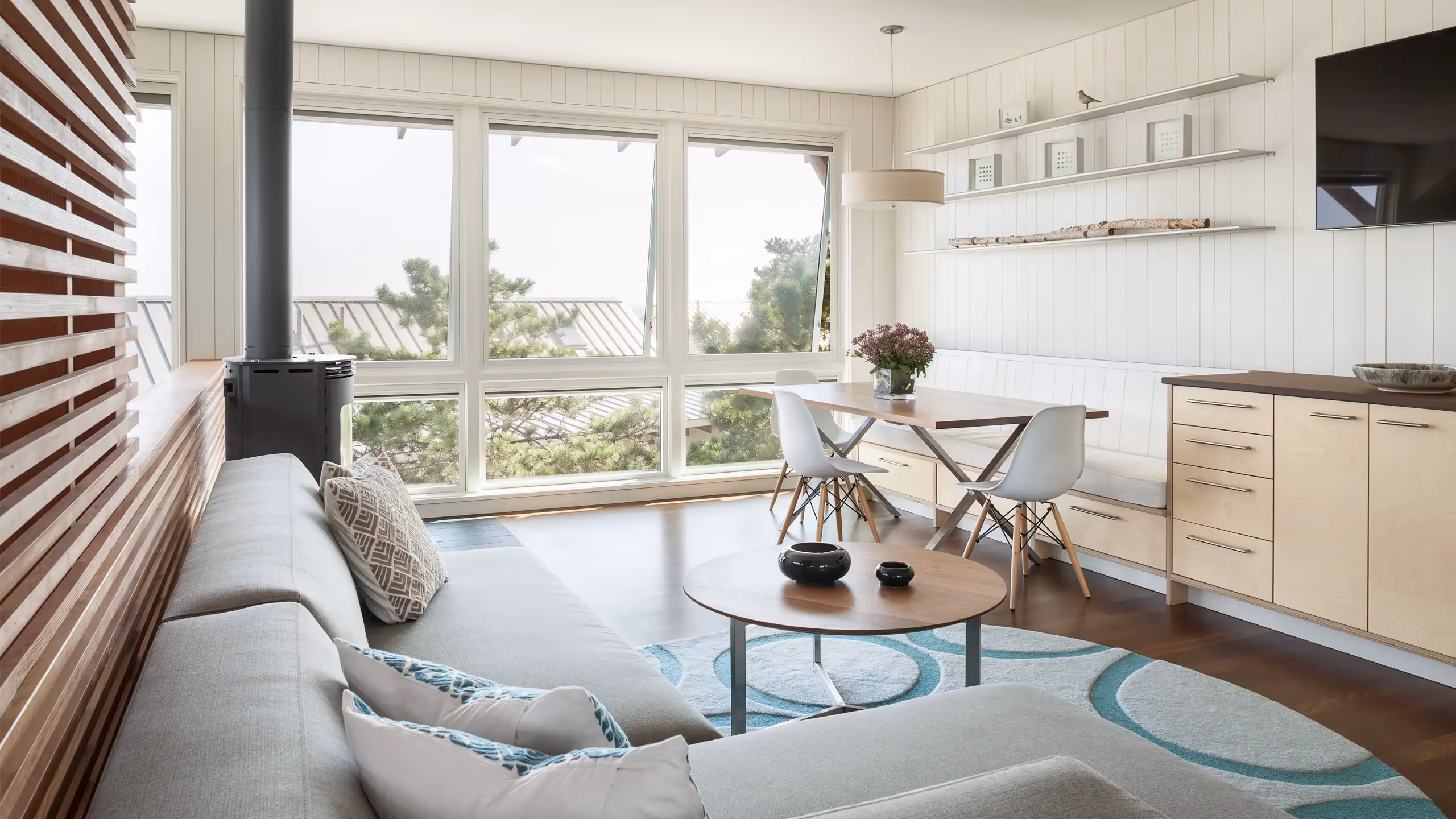 Modern minimalist living room with large windows, wood stove, and blue rug
