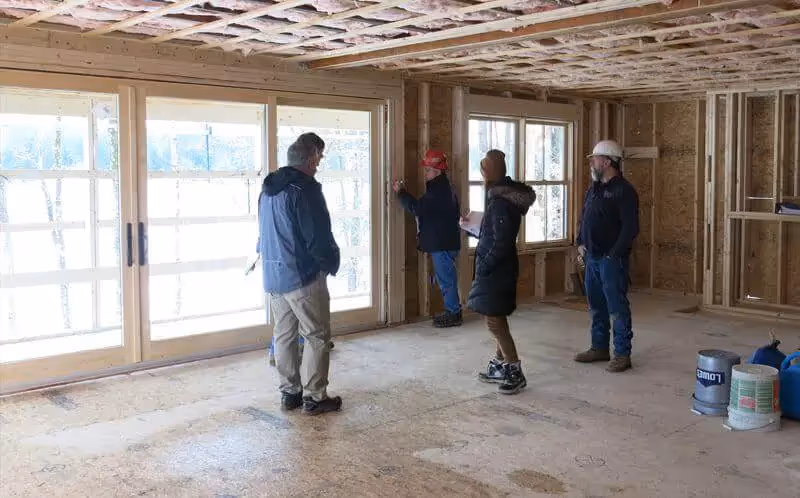Construction workers discussing project inside unfinished house with large windows