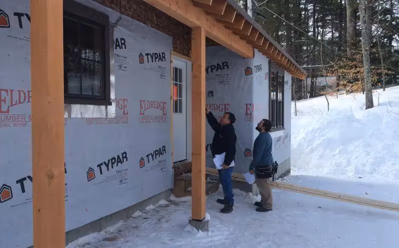 Workers installing house wrap on snowy winter construction site