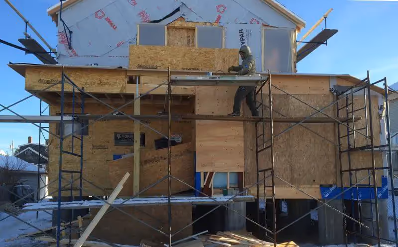 House under construction with scaffolding and wooden framing on a winter day