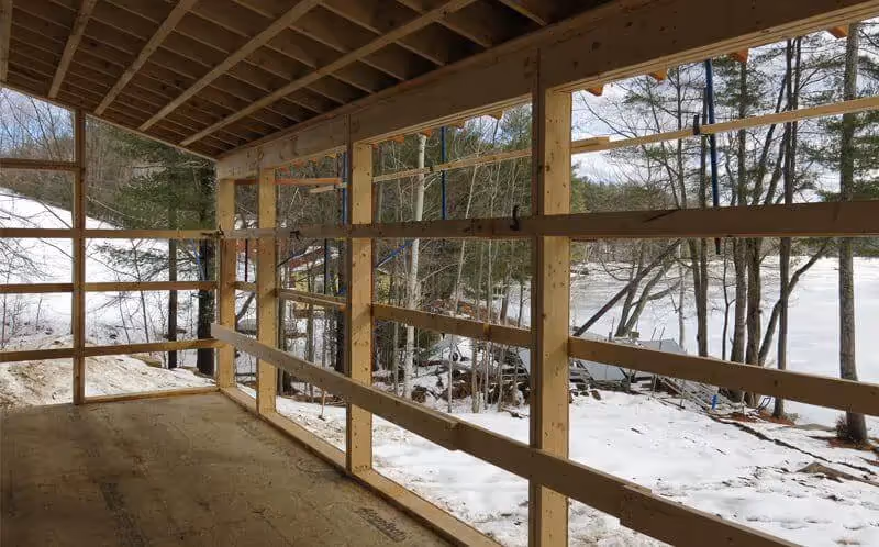 Wooden framed structure with large windows overlooking snowy winter forest landscape