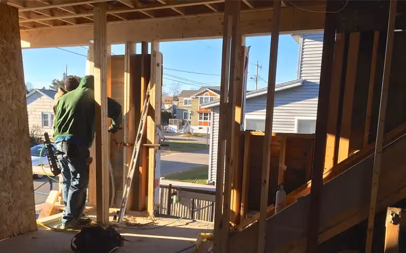 Construction worker framing interior of house with neighborhood view