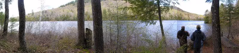 Two hikers overlooking a serene lake surrounded by forest and hills
