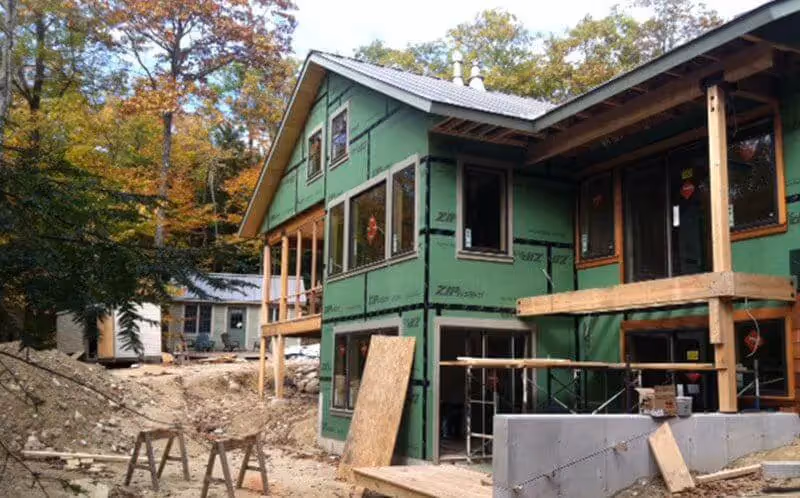 Green wooden house under construction with wooden scaffolding in forest