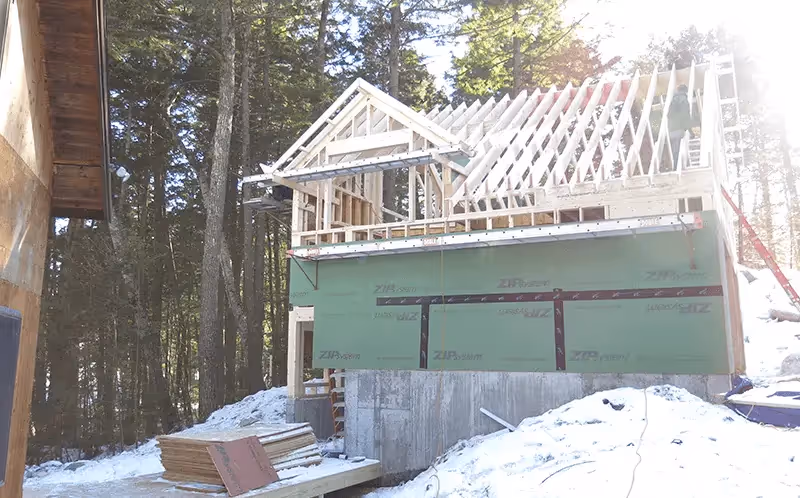 Wooden house frame under construction in snowy forest setting