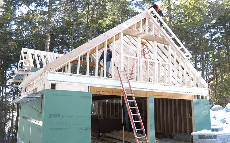 Wooden house frame under construction with ladders in forest setting