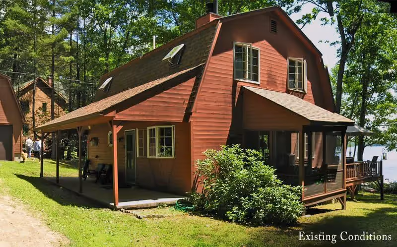 Red wooden cabin with porch nestled in green forest surrounded by trees
