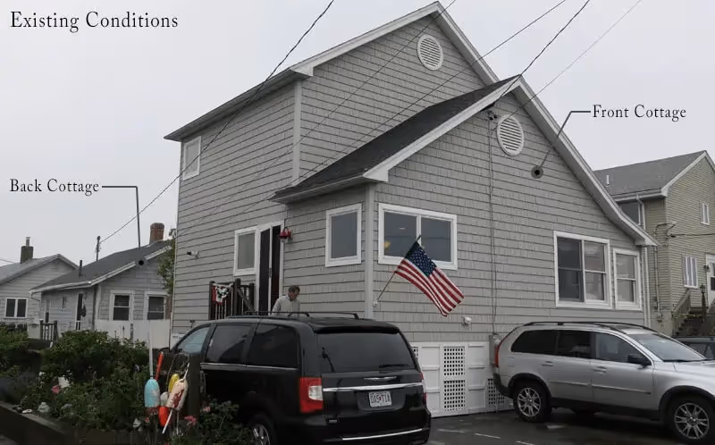 Gray coastal cottage with American flag, parked cars, and front and back sections