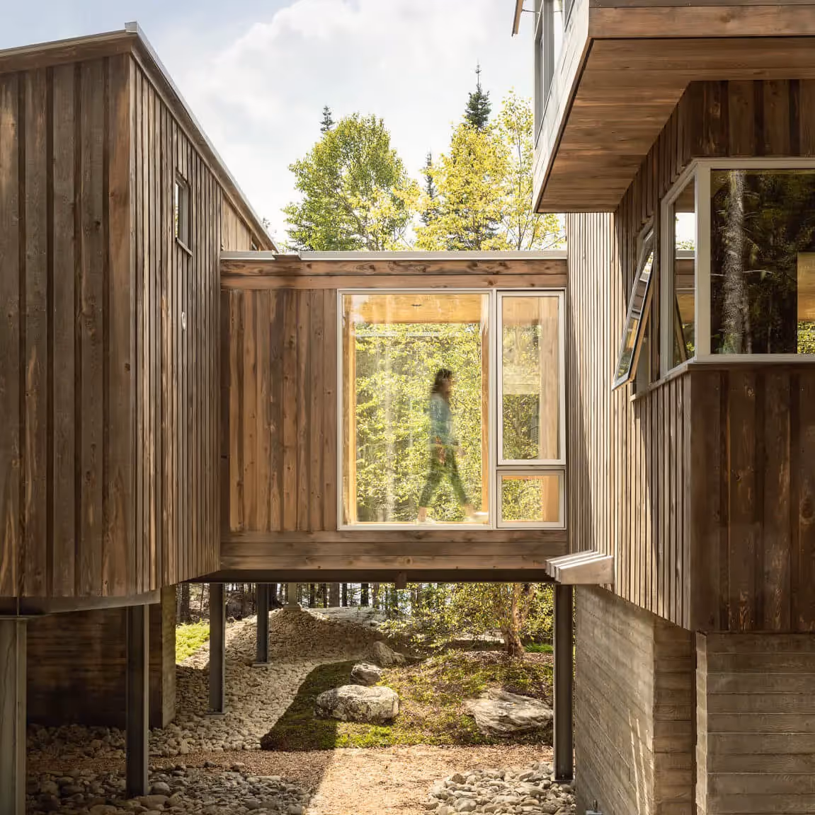 Wooden cabin with large windows, silhouette walking through forest backdrop
