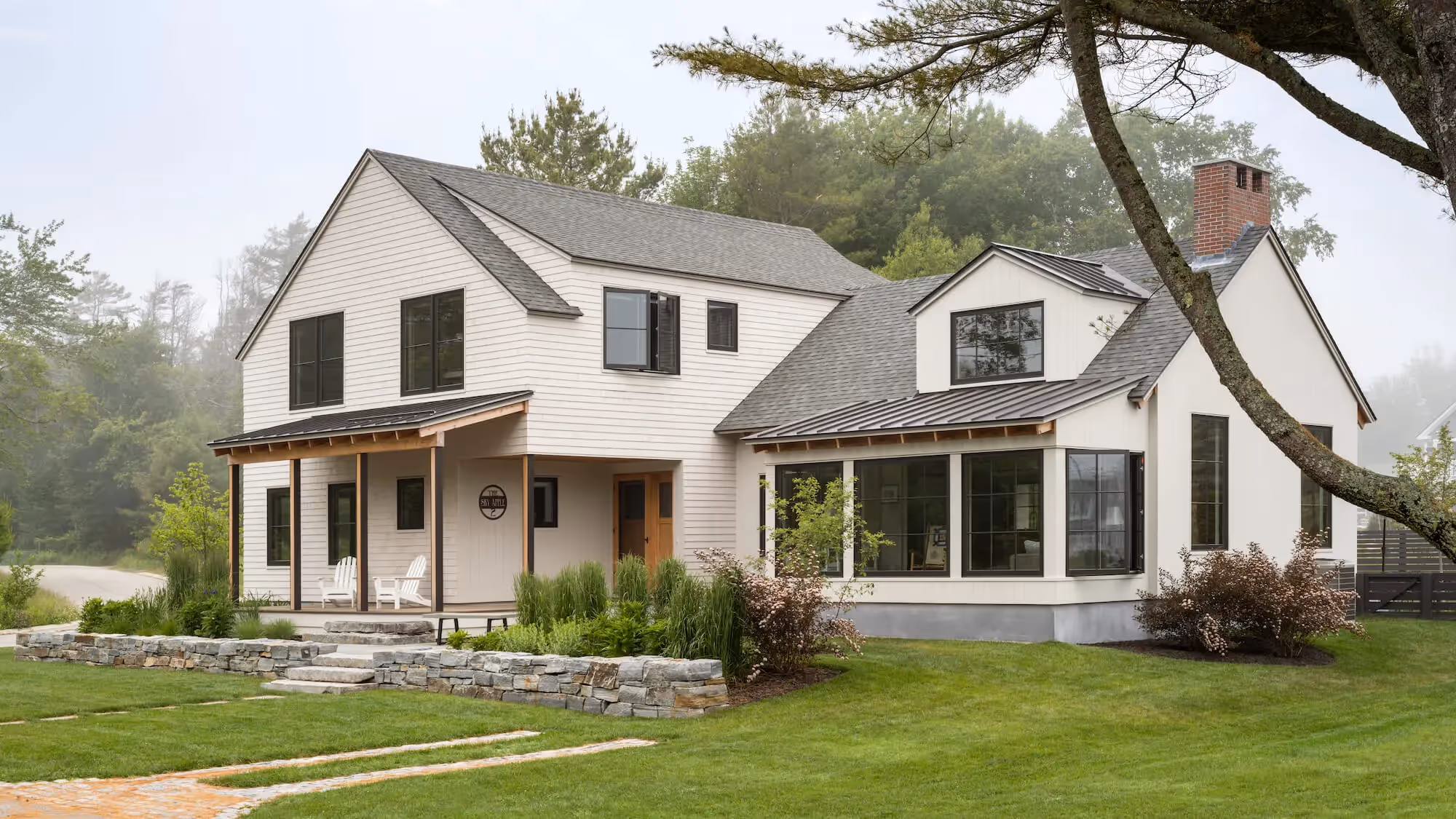 Modern farmhouse with white exterior, porch, and stone landscaping in misty setting